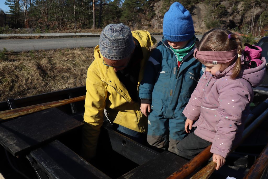 Nicolay (5) og Ronja (5) følger nøye med når Thor åpner ei luke i båten og viser hvor en kan oppbevare fiskefangsten i vann om bord.