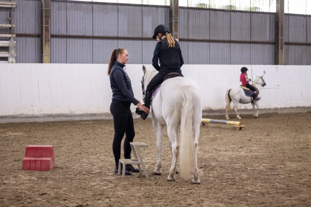God veiledning er viktig for å lykkes med ridningen. Stallmedarbeider Camilla hjelper til med å tilpasse utstyret til hest og rytter.